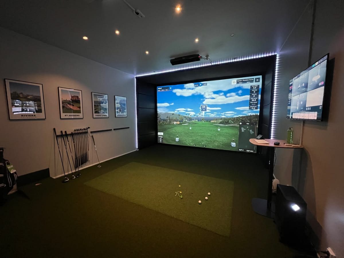 Basement golf simulator with LED-lit screen and framed course prints